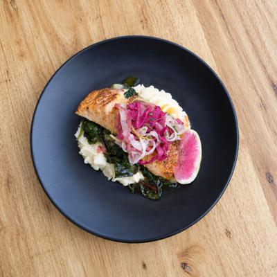 Salmon Al Limone served over greens and mashed potatoes, topped with pickled onions.