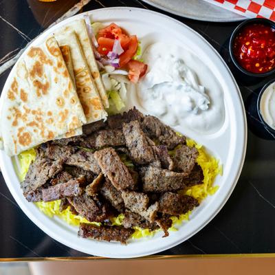 Lamb kebab on a bed of saffron rice, with tzatziki, salad, and pita bread.
