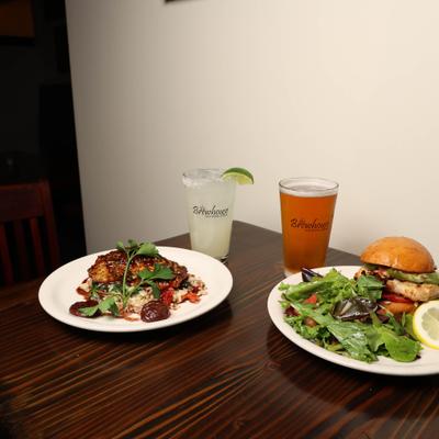 plate of Grilled salmon and plate of Grilled Chicken sandwich with house salad , Beer and margarita.