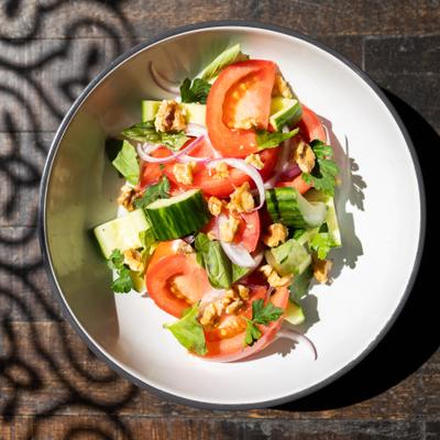 traditional georgian salad of tomatoes and cucumbers with fresh herbs in white bowl