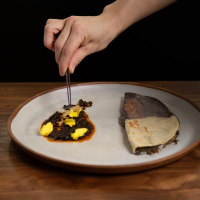 Hand is using tweezers to add a garnish to the side dish, alongside taco.