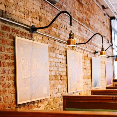 Restaurant interior with brick walls, framed art, industrial lighting, and booth seating.