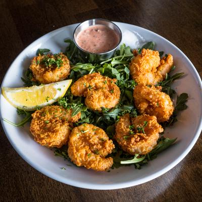 Fried shrimp served on a bed of arugula with creamy sauce and a lemon wedge.