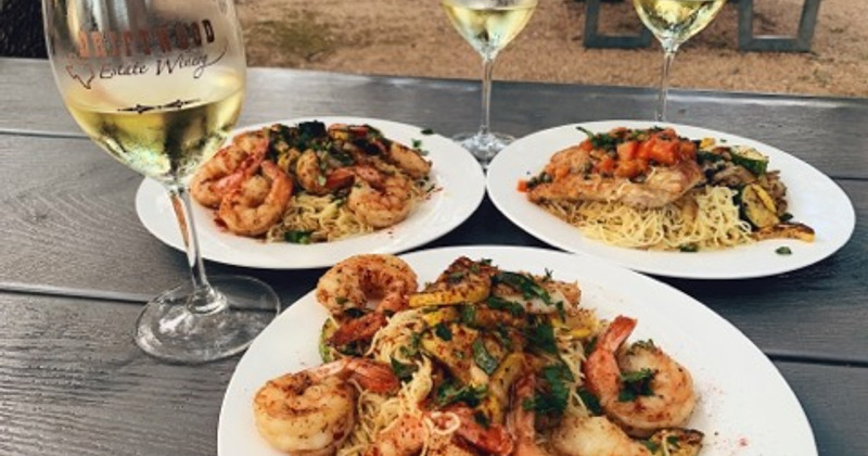 Three plates outdoors on a table with shrimp and chicken meals.