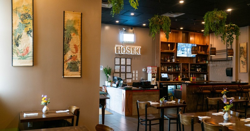 A warmly lit interior - a wooden bar, hanging plants, Asian-inspired wall art, dining tables