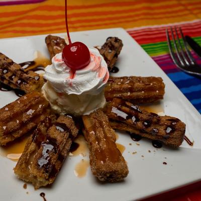 Churros with ice cream, whipped cream, chocolate drizzle, and maraschino cherry.