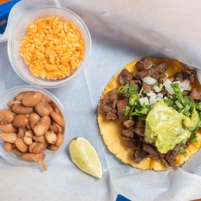 Taco with diced beef, onions, cilantro, and guacamole, served with cups of rice and beans.