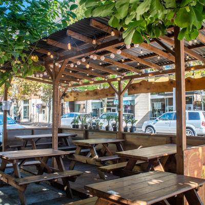Outdoor dining area with picnic tables under a wooden pergola and string lights.