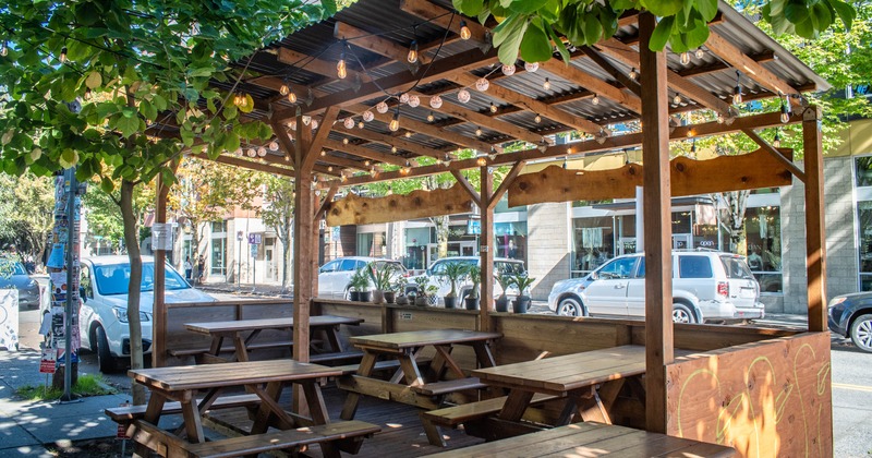Outdoor dining area with picnic tables under a wooden pergola and string lights