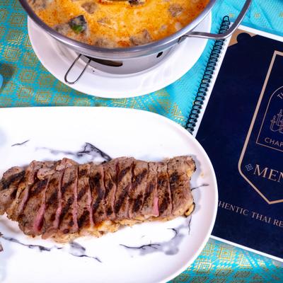 Crying Tiger Steak served alongside a bowl of curry, overhead view.