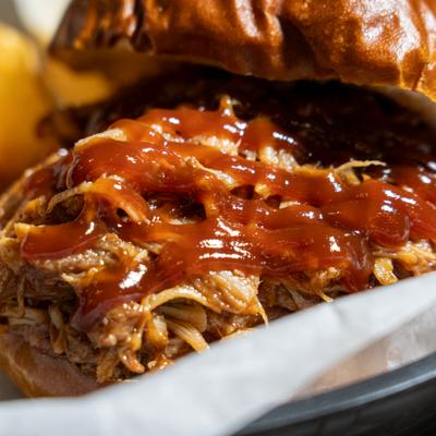 Close-up of a barbecue pulled pork sandwich on a toasted bun, drizzled with barbecue sauce.