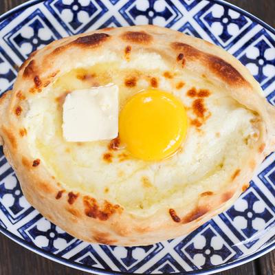 georgian cheesebread (khachapuri) with egg and butter, on blue and white plate