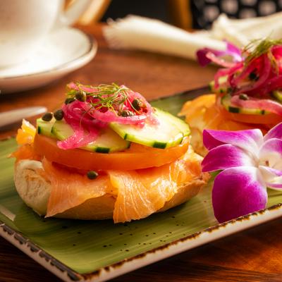 Lox bagel on a green plate, garnished with a purple orchid flower.