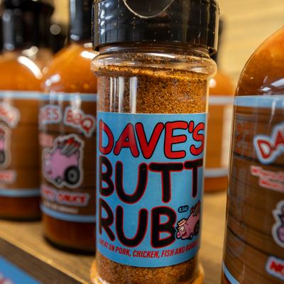 A shaker of Dave's Butt Rub seasoning sits on a shelf with Dave's BBQ sauce bottles.