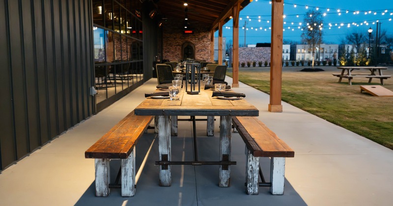 Outdoor dining area with rustic wood table and benches under string lights