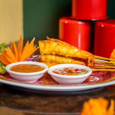 Grilled shrimp skewers served on a plate with two colorful dipping sauces.