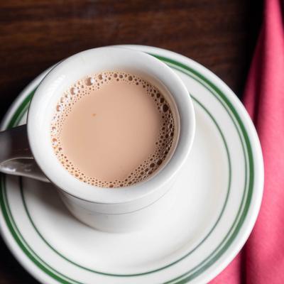 White cup of chai rests on a white plate with green stripes.