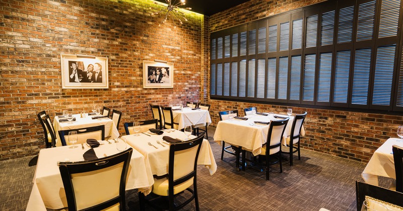 A stylish restaurant interior with brick walls, and white tablecloth-covered tables