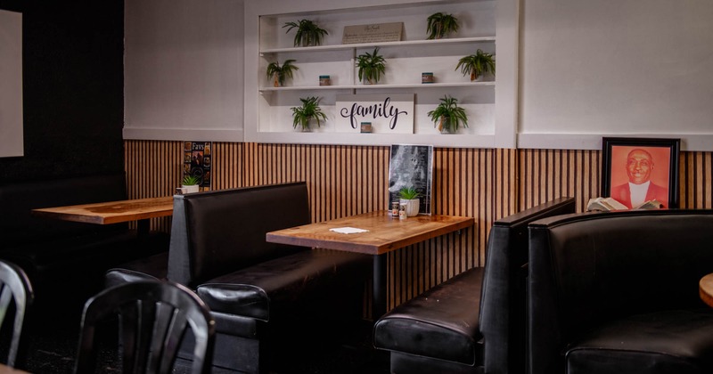 Restaurant interior with black booths, wooden tables, and decorative plants