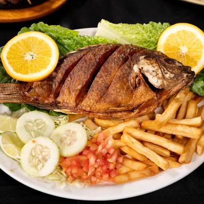 Whole fried tilapia served with fries, fresh vegetables and garnishes.