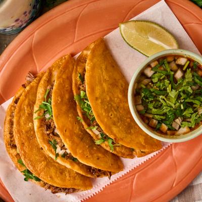 Top-down view of birria tacos with a side of dipping broth.