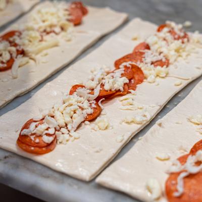 Pizza dough strips topped with pepperoni and shredded cheese prepared for baking.