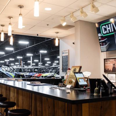 Interior, counter with bar stools, wide showroom with parked off-road vehicles.