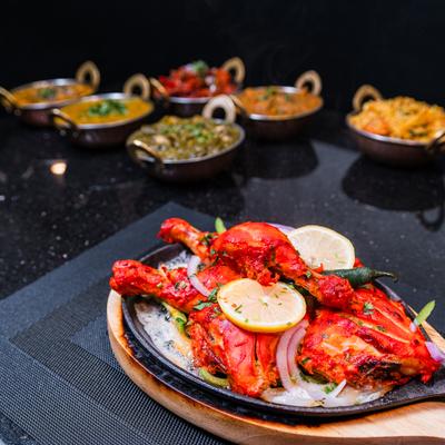 Tandoori chicken served on a sizzling plate with warious side dishes in the background.
