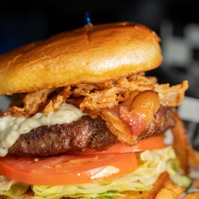 A burger topped with crispy onions and tomatoes.