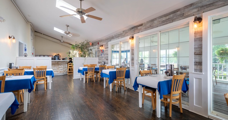 Inside, blue tablecloths, wooden chairs, and large glass doors, featuring a stone counter