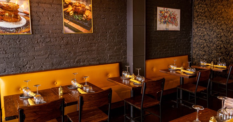 Cozy interior - orange cushioned bench, dark wooden tables and framed photos on a brick wall