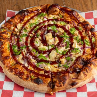 A pizza topped with green peppers, onions, chicken, and a spiral of barbecue sauce.
