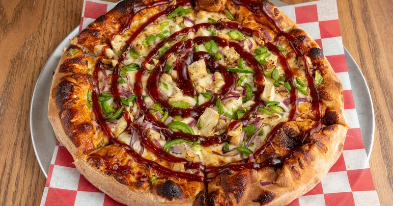A pizza topped with green peppers, onions, chicken, and barbecue sauce