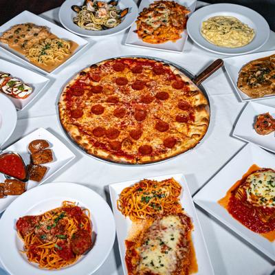 Various  Italian dishes spread on a table with a pepperoni pizza in the center.