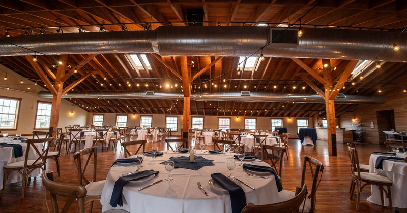 Banquet hall - wooden beams, string lights, neatly arranged tables - white tablecloths, blue napkins