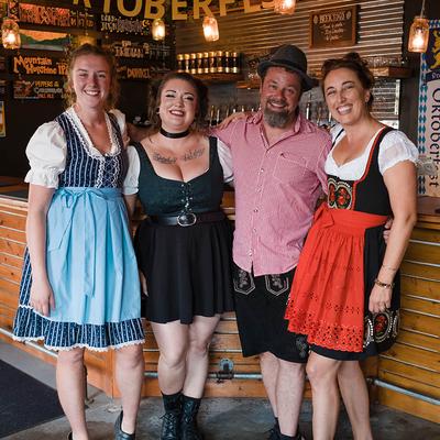 Four people in Oktoberfest-style outfits posing inside a bar.