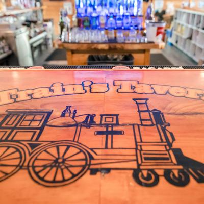 Wooden bar top with an engraved train illustration and blurred liquor bottles in the background.