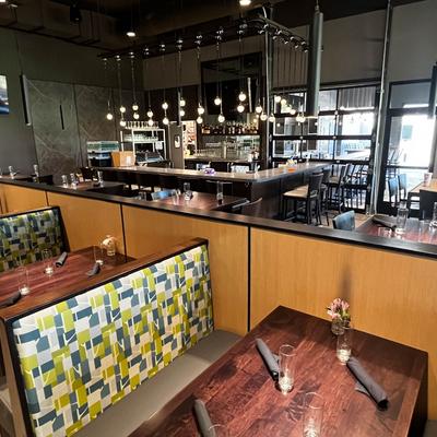 Modern restaurant interior with wooden tables and colorful patterned booth seating.