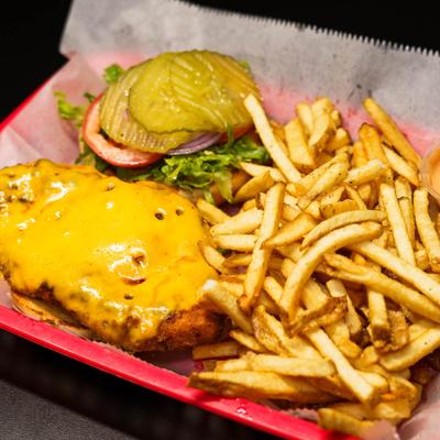 Fried chicken sandwich, with melted cheese, hot sauce, lettuce, tomato, pickles, and fries.