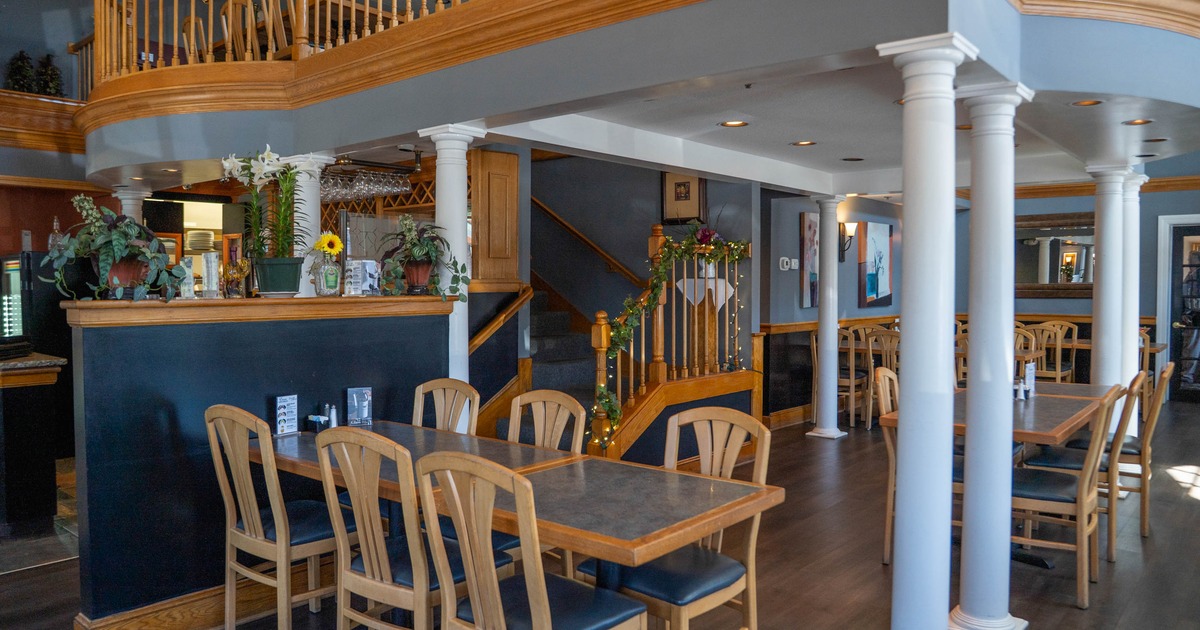 Interior of a restaurant with wooden furniture, white columns, and a decorated staircase