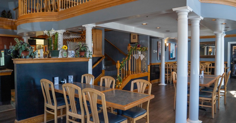 Interior of a restaurant with wooden furniture, white columns, and a decorated staircase