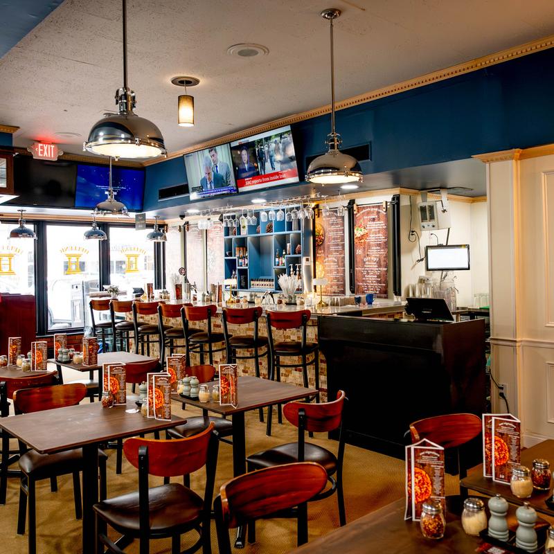 Interior of a modern restaurant with tables, chairs, a bar area, and hanging pendant lights