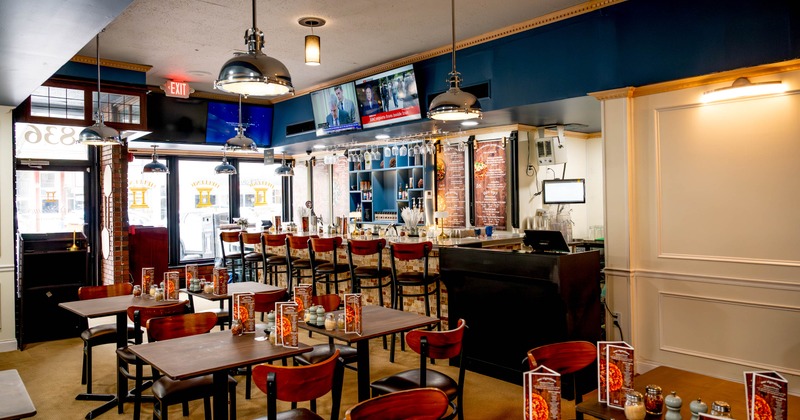 Interior of a modern restaurant with tables, chairs, a bar area, and hanging pendant lights
