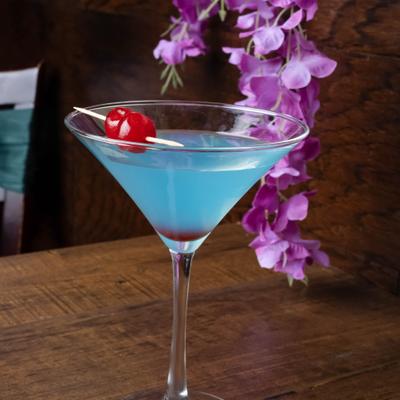Blue cocktail garnished with cherrys on a pick, served in martini glass.