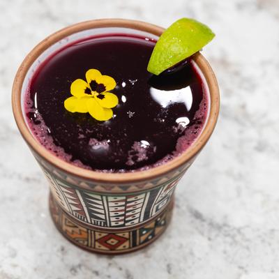Peruvian purple corn drink in a hand-painted clay mug with lime and flower garnish.
