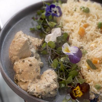 Dish of chicken with herbed rice, garnished with microgreens and edible flowers.