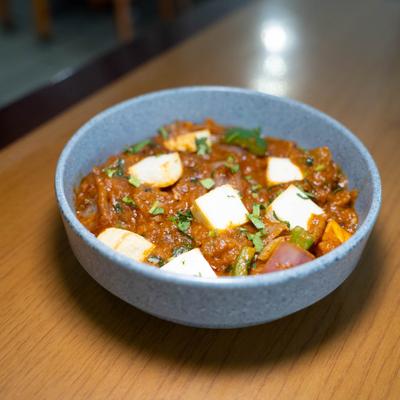 Bowl of paneer curry topped with herbs.