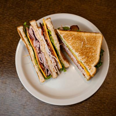 Club sandwich cut into toasted halves on a white plate.