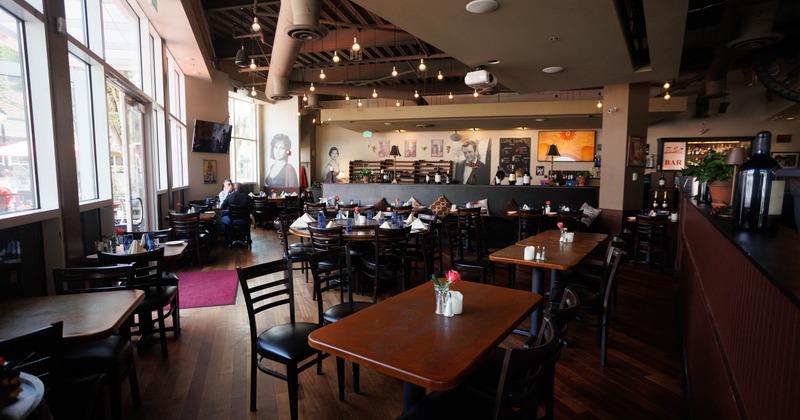 Interior view of a restaurant featuring wooden tables, black chairs, and large windows