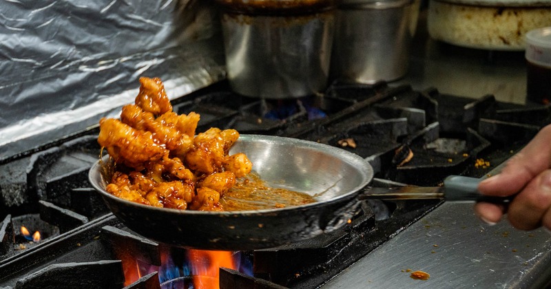 Chef cooks glazed chicken in a sizzling pan over a gas stove